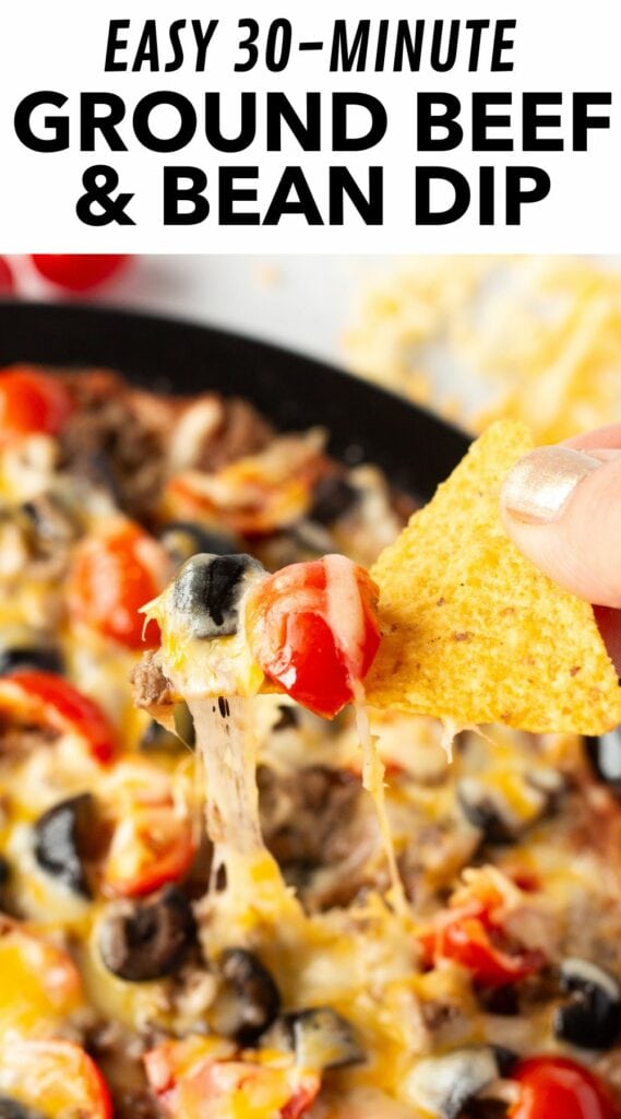 pin for ground beef and bean dip, showing a tortilla chip pulling a portion of the dip away from a plate.