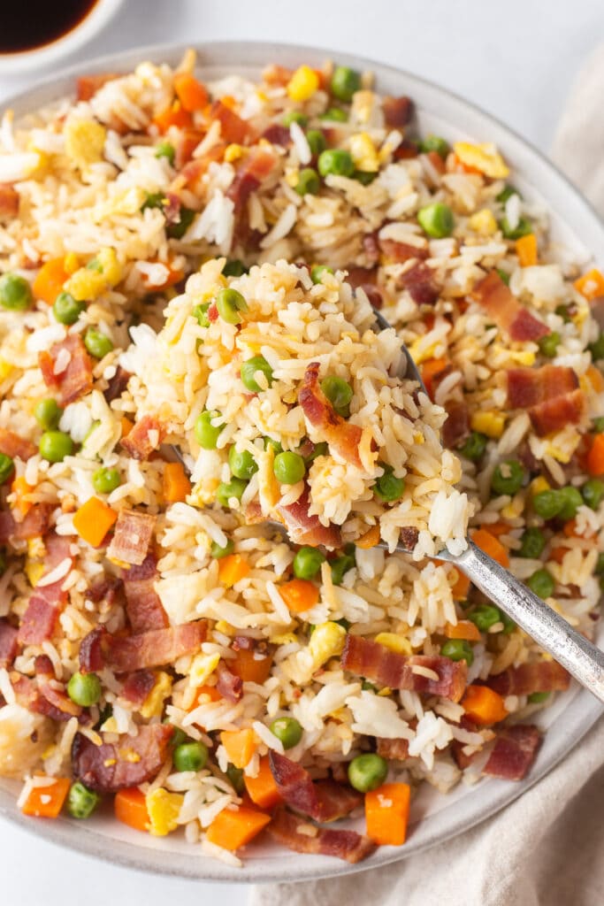 Top down shot of a large bowl of bacon rice with a large serving spoon taking a scoop out of it.