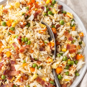 Top down shot of a large bowl of bacon rice with a large serving spoon in the middle of the bowl.