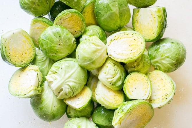 Close up of Brussels sprouts halved and seasoned in a bowl.