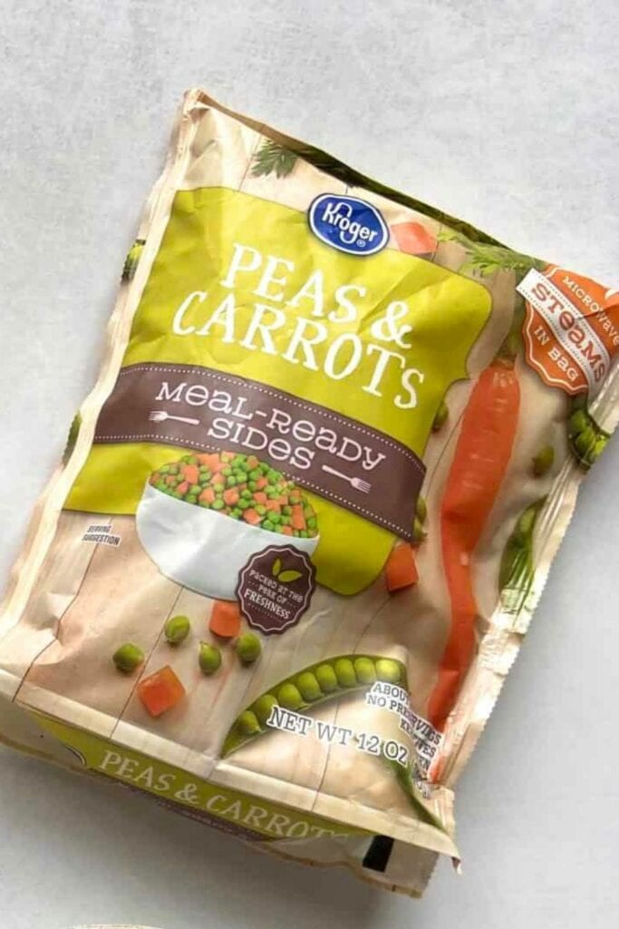 Close up of a bag of frozen peas and carrots on a light gray background.