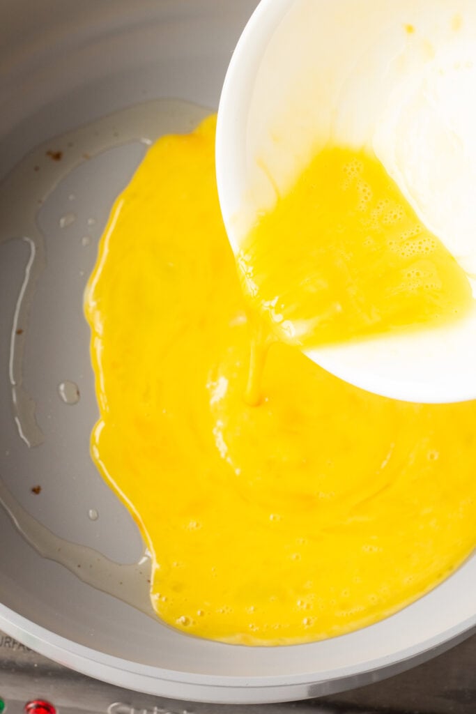 Pouring raw mixed eggs into a frying pan.