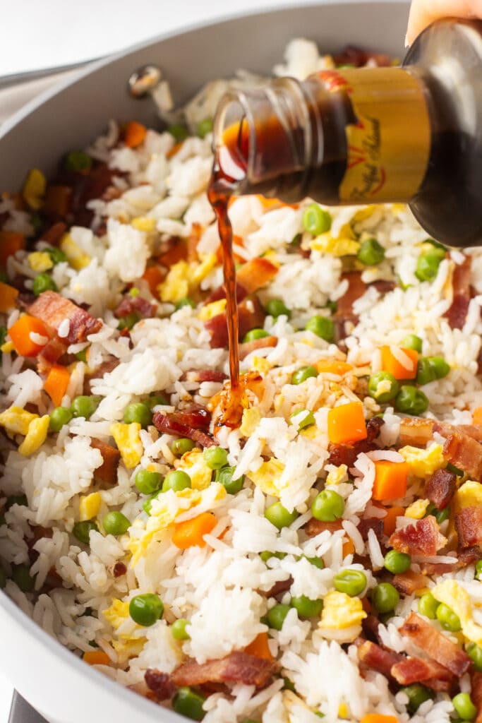 Pouring tamari sauce into a large pan with bacon fried rice in it.