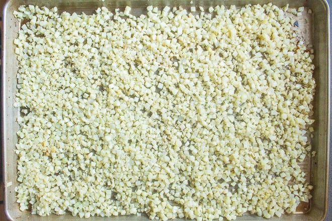 Raw cauliflower rice in a single layer on a large sheet pan.