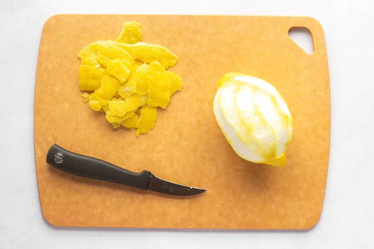 a lemon that's been peeled on a cutting board with pieces of lemon skin and a paring knife.