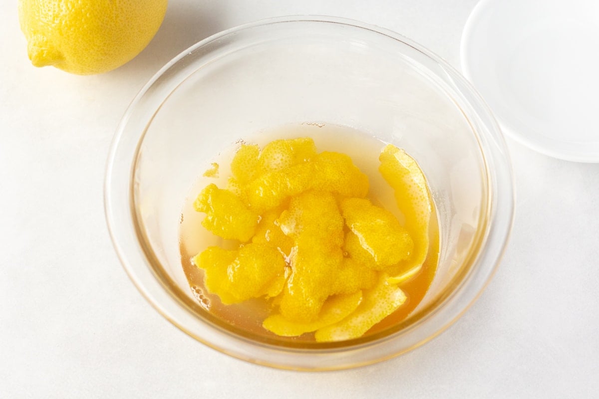 a clear bowl with lemon syrup and pieces of lemon skin sitting in it.