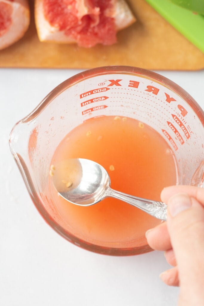 a spoon removing seeds from freshly squeezed grapefruit juice in a measuring cup.