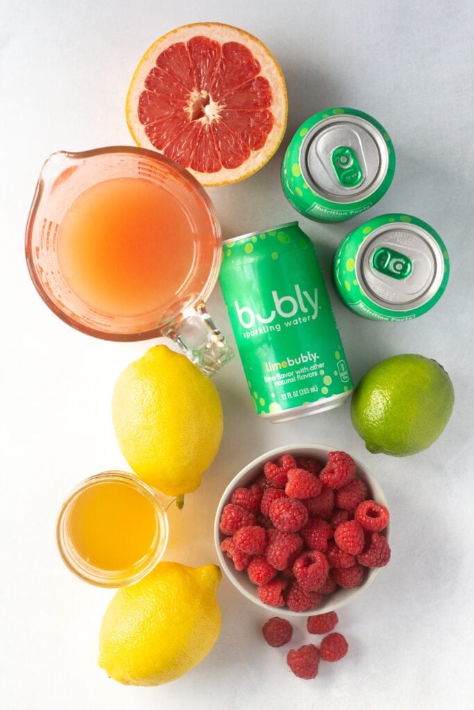top down shot of lemons, grapefruit, limes, raspberries, juices, and cans of lime sparkling water.