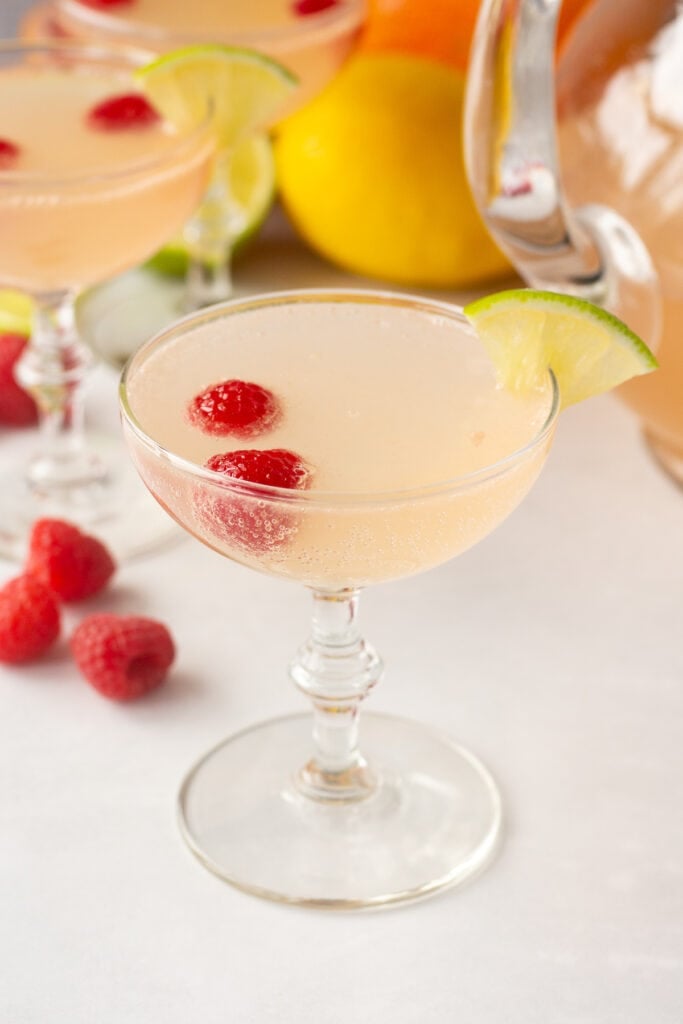 a pink mocktail in a champagne glass with citrus fruit and raspberries in and around it.