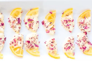 Two lines of candied lemon slices with half of them covered in white chocolate and pink rose petals on a white plate.
