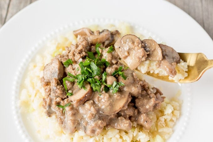 Ground beef stroganoff over cauliflower rice with a fork lifting a bit off a white plate.