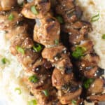 Top down shot of grilled teriyaki chicken skewers on top of a bed of white rice.