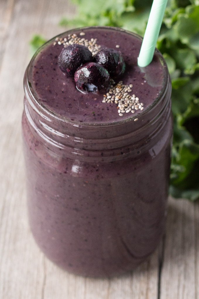 small clear jar of kid friendly blueberry kale smoothie with green kale in background and seafoam green straw