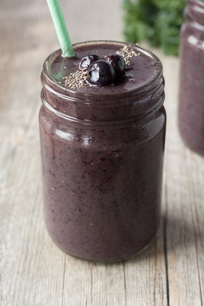 blueberry kale smoothie in a jar with a seafoam green straw