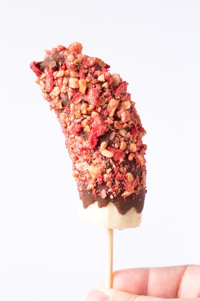 peanut butter jelly chocolate covered frozen banana pop being held up straight