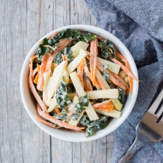 top down shot of kohlrabi, kale, and carrot coleslaw in a white bowl with a fork and gray towel