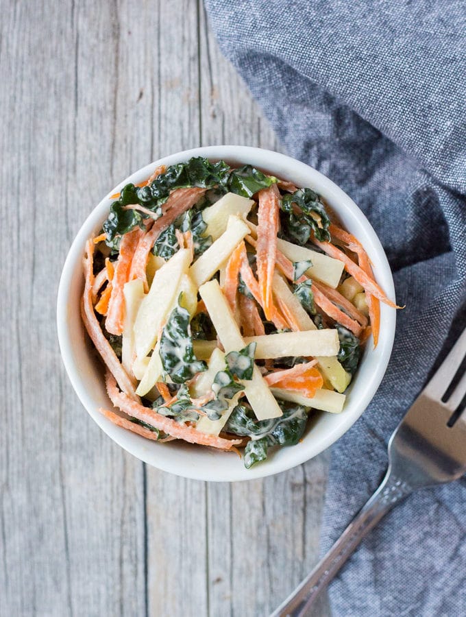 top down shot of kohlrabi, kale, and carrot coleslaw in a white bowl with a fork and gray towel