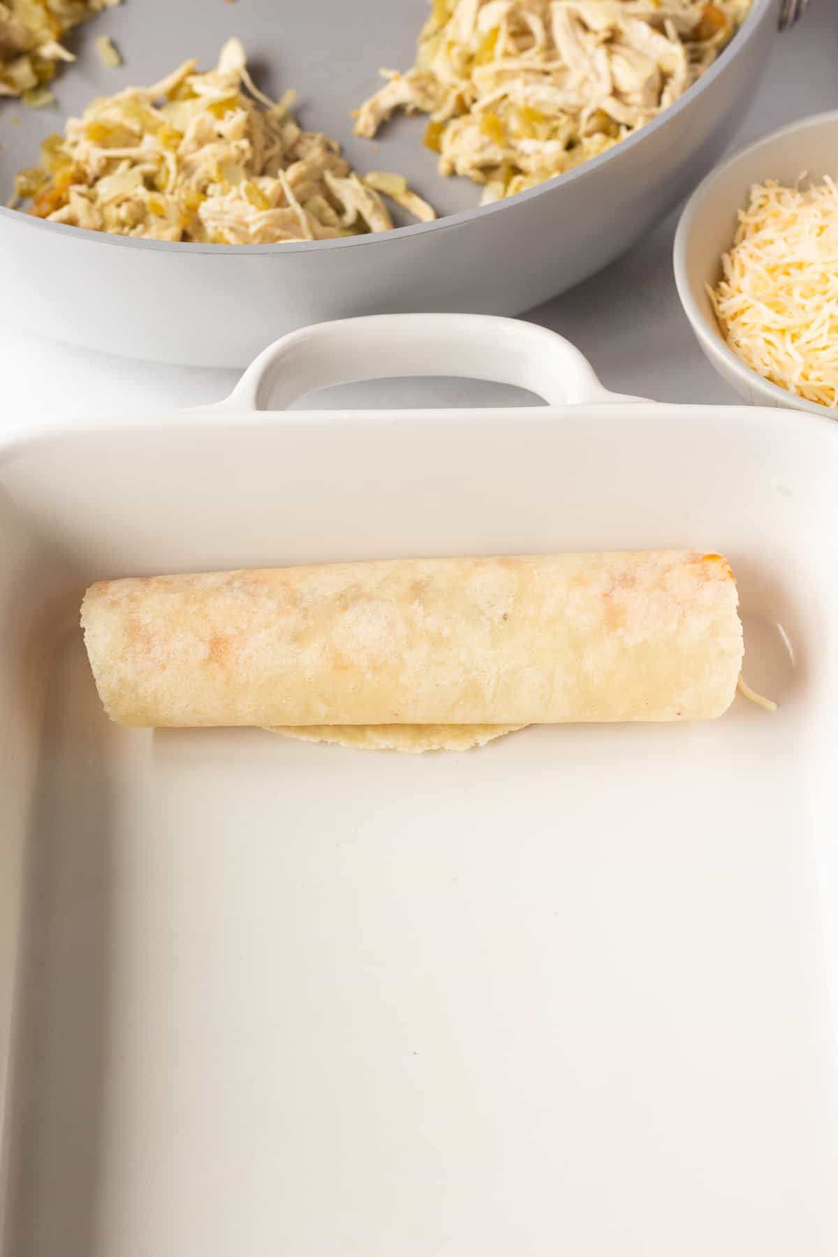 A rolled up tortilla with chicken and enchilada sauce in it, in a white casserole dish.