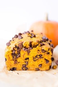 Straight on shot of a loaf of chocolate chip pumpkin bread that's been cut into. A small pumpkin is in the background.