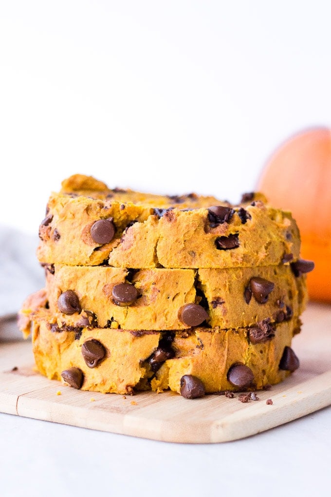 three slices of chocolate chip pumpkin bread stacked on top of each other, on a wood cutting board