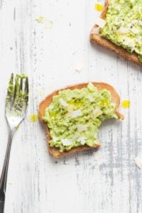 Pieces of avocado toast with a bit out of the bottom right corner. a fork is the left with avocado on the tines and another piece of toast is in the upper right corner.