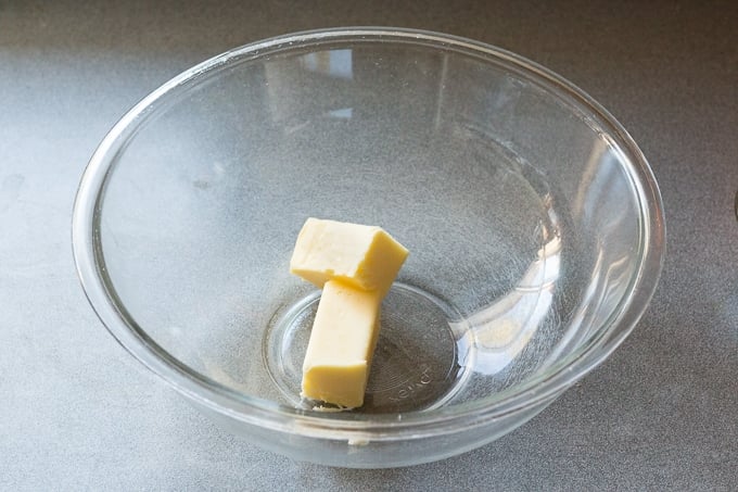 A halved stick of butter in a large, clear microwavable bowl.