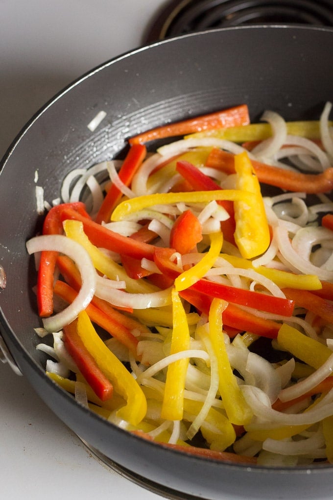 sliced onion and red and yellow bell peppers in a frying pan