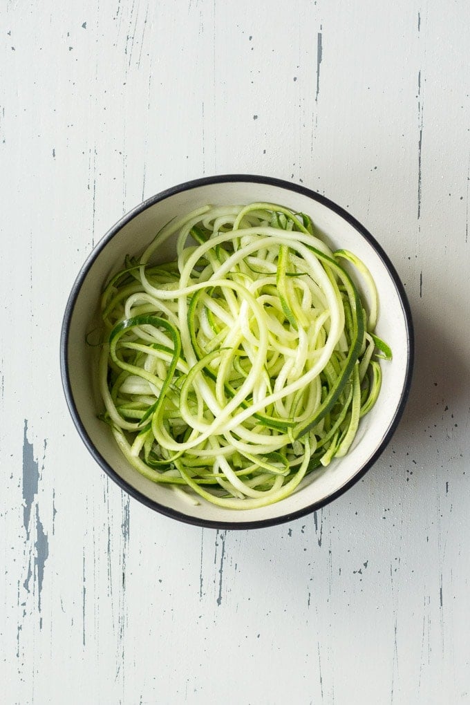 top down view of zucchini noodles in a bowl on an off-white background
