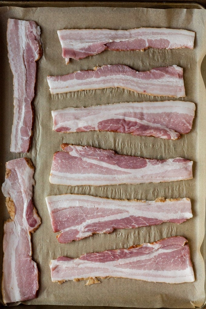top down view of 8 raw bacon slices on top of parchment paper in a sheet pan