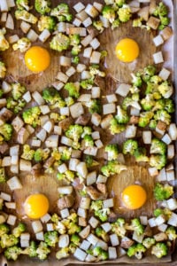 top down view of 4 eggs in wells with cubed pototoes and romanesco on a sheet pan