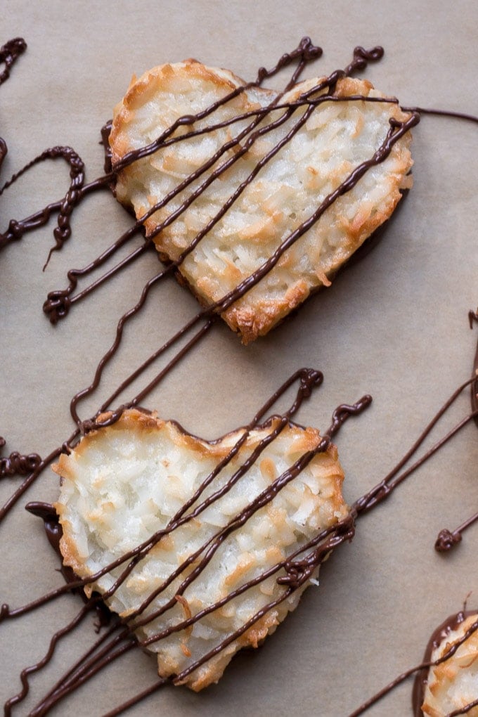 top down view of chocolate drizzled on top of gluten free coconut macaroons in heart shapes on parchment paper
