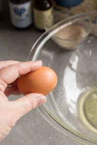 zoomed in view of a hand holding an egg against the rim of a large pyrex bowl