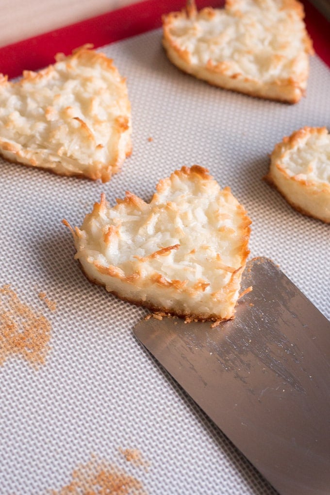 zoomed in view of a flat metal spatula sliding under a chewy coconut macaroon heart cookie