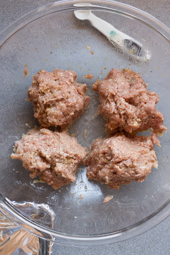 A mixture for baked paleo turkey meatballs separated into 4 sections in a glass bowl on a gray countertop.