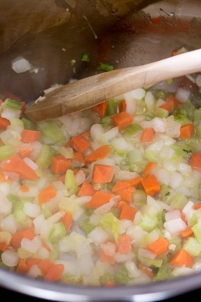 Mirepoix mix being cooked in an Instant Pot with a wooden spoon.