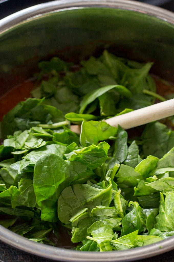 Shredded spinach being added to soup in an instant pot.