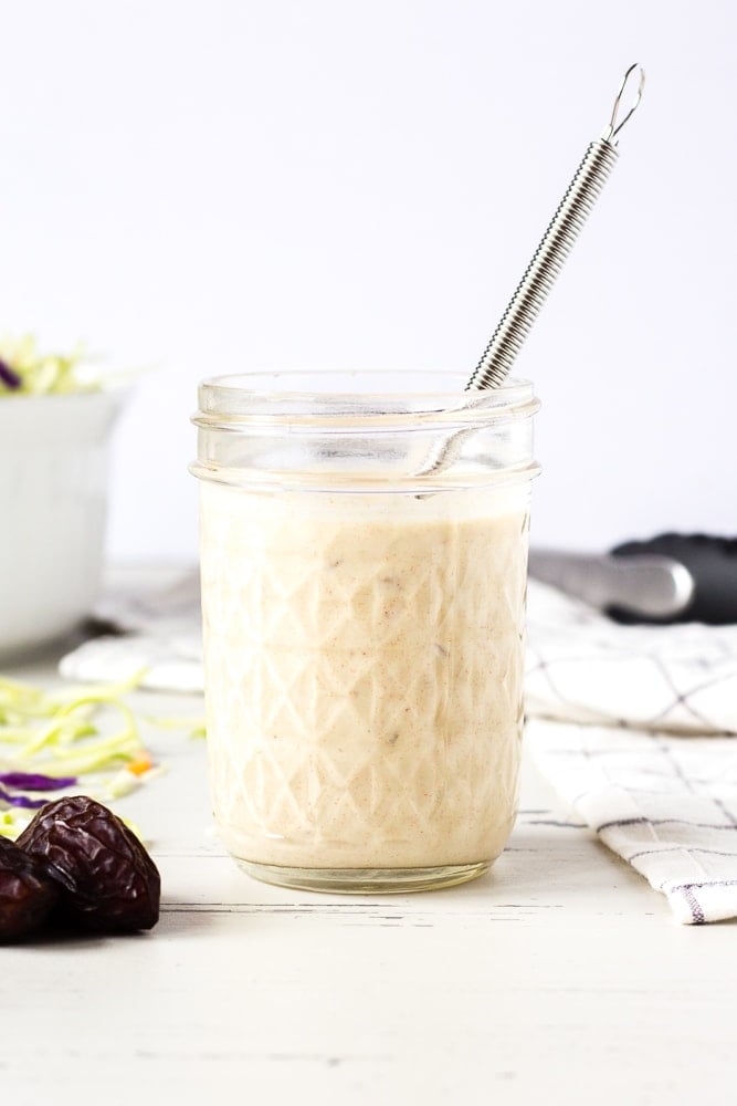 Straight on shot of healthy coleslaw dressing in a mason jar with slaw and dates around it.