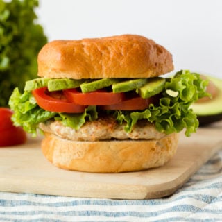 straight on shot of a healthy ground chicken burger with fixing in the background on top of a cutting board