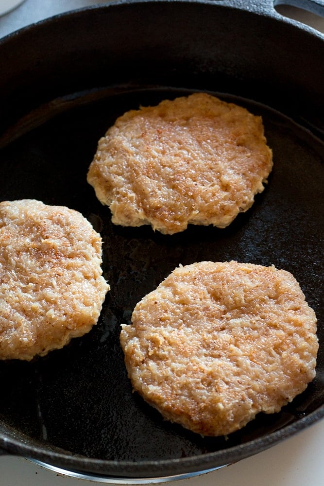 cooking three healthy ground chicken burgers in a cast iron skillet
