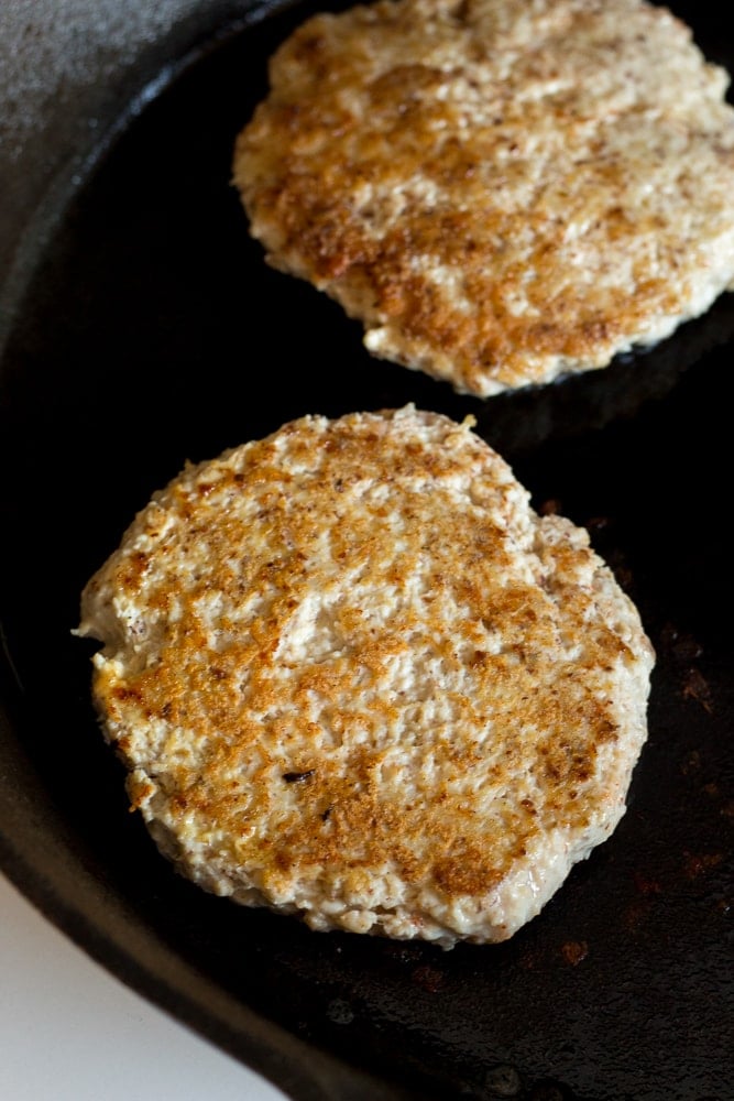 a healthy ground chicken burger flipped over and cooking in a cast iron skiller