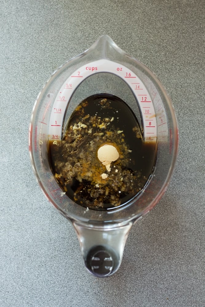 Top down shot of a liquid measuring cup with coconut aminos and balsamic vinegar, garlic, and ground ginger in it.