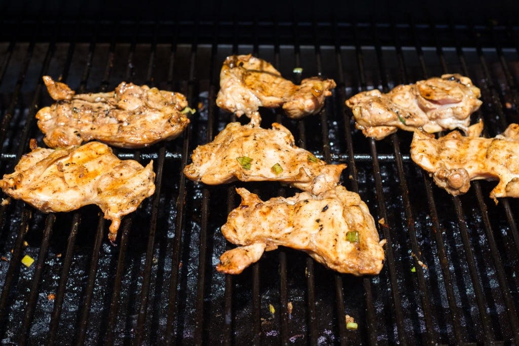 Close up of boneless skinless chicken thighs cooking on a grill.