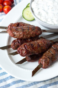lamb kababs on a white plate with dip in a bowl