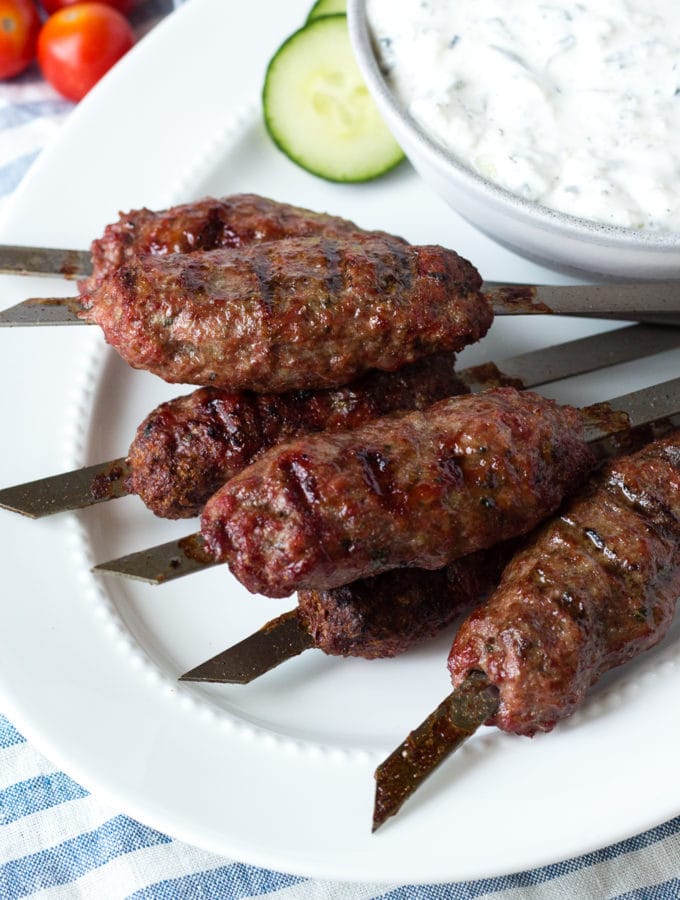 lamb kababs on a white plate with dip in a bowl