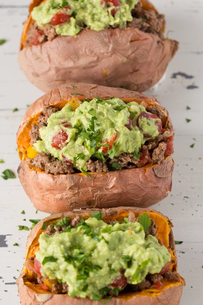 Three stuffed sweet potatoes with ground beef and guacamole on a light wooden background.