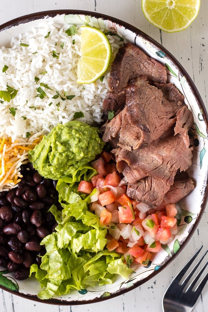Zoomed in shot of ingredients for a steak burrito in a large bowl with a fork in the right bottom corner.