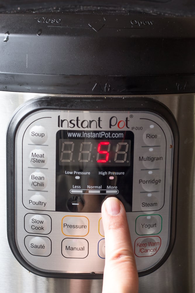 A finger pressing a button on the Instant pot to set the time to 5 minutes.