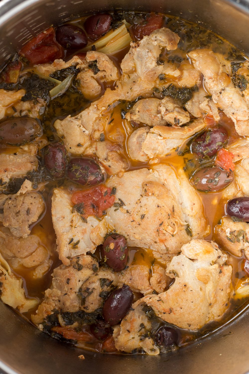 Top down shot of cooked greek chicken thighs in an Instant Pot with kalamata olives, artichoke hearts, and diced tomatoes.