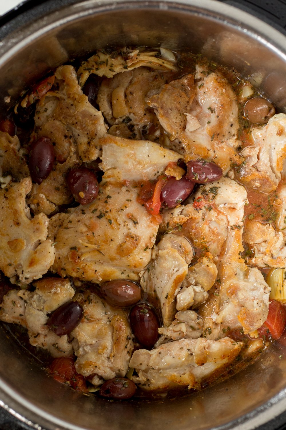 Uncooked chicken thighs with kalamata olives, artichocke hearts, and tomatoes in an Instant Pot.