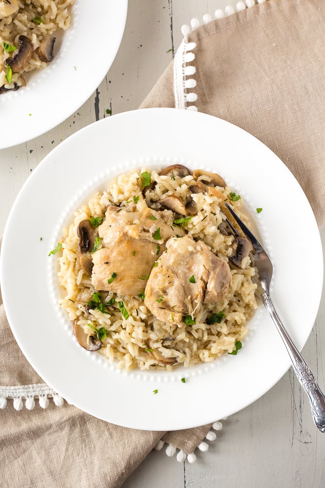 Top down shot of boneless chicken thighs and rice with mushrooms on a white plate. A fork also rests on the plate and a brown napkin is under the plate.